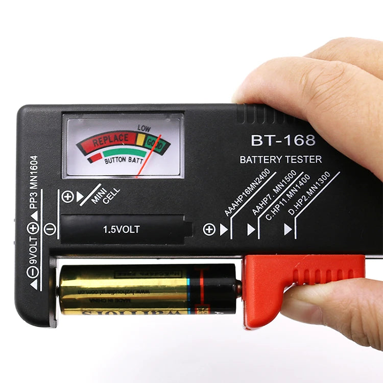 A hand holds a black battery tester device with a color-coded indicator and a battery inserted.