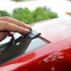 A hand is applying a black sealing strip to the edge of a red car window or roof.