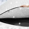 A hand is holding a black universal car windshield sunshade and snow protector against a white surface in snowy conditions.