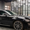 A glossy black car is parked in a modern showroom with large glass windows.