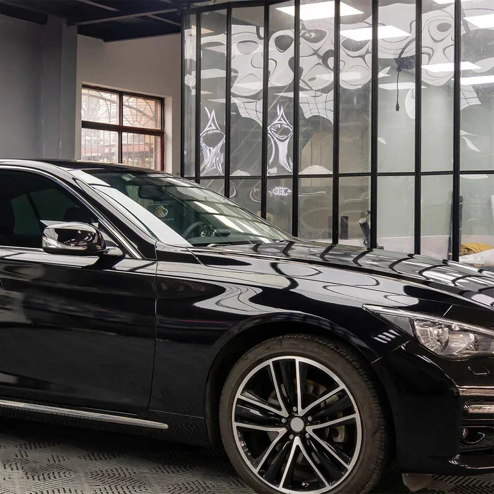 A glossy black car is parked in a modern showroom with large glass windows.
