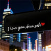 Gros plan d'un rétroviseur de voiture affichant "I love you drive safe" avec un cœur rouge sur fond sombre.