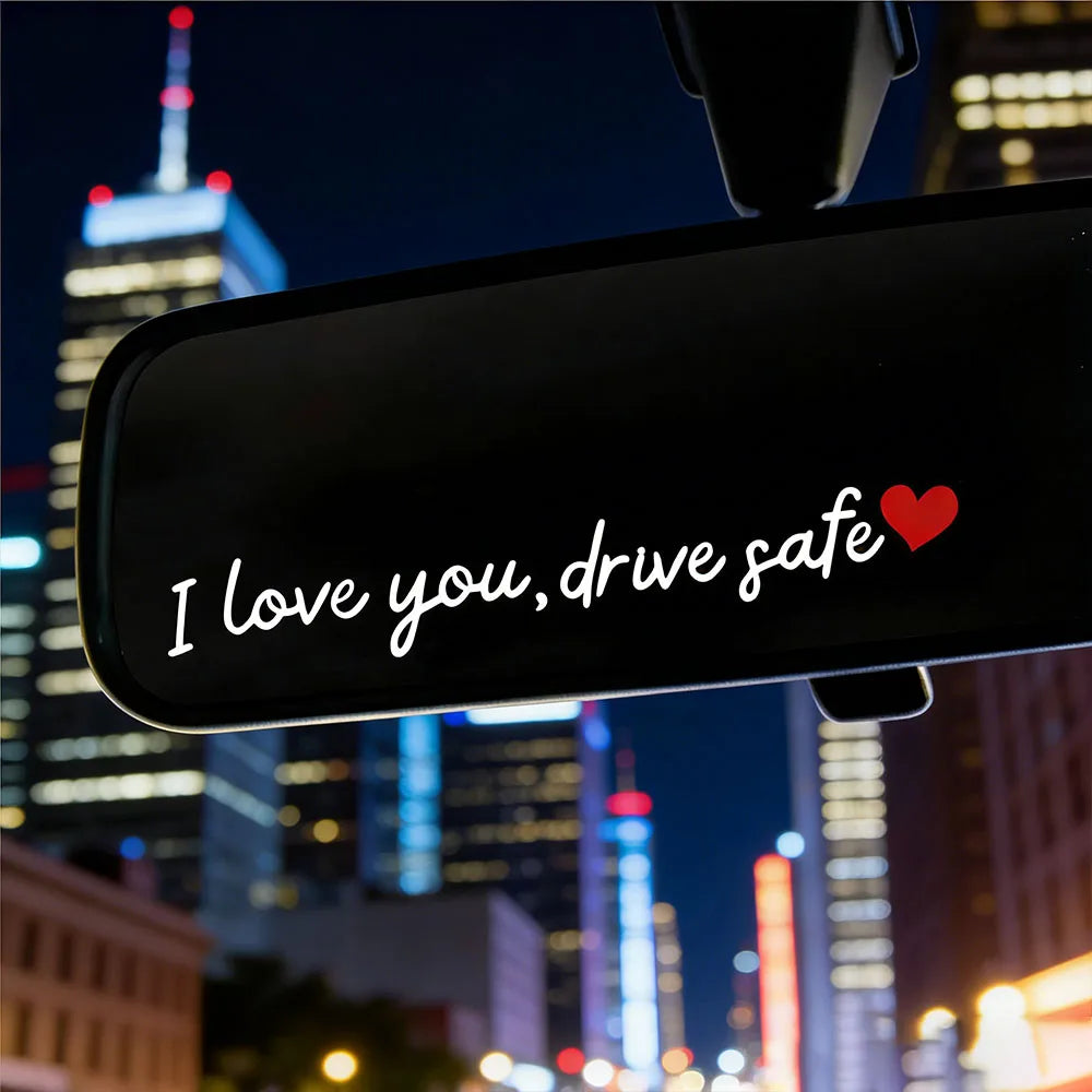 Gros plan d'un rétroviseur de voiture affichant "I love you drive safe" avec un cœur rouge sur fond sombre.