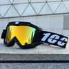 A pair of black windproof sports goggles with yellow-tinted lenses resting on a gray stone surface.