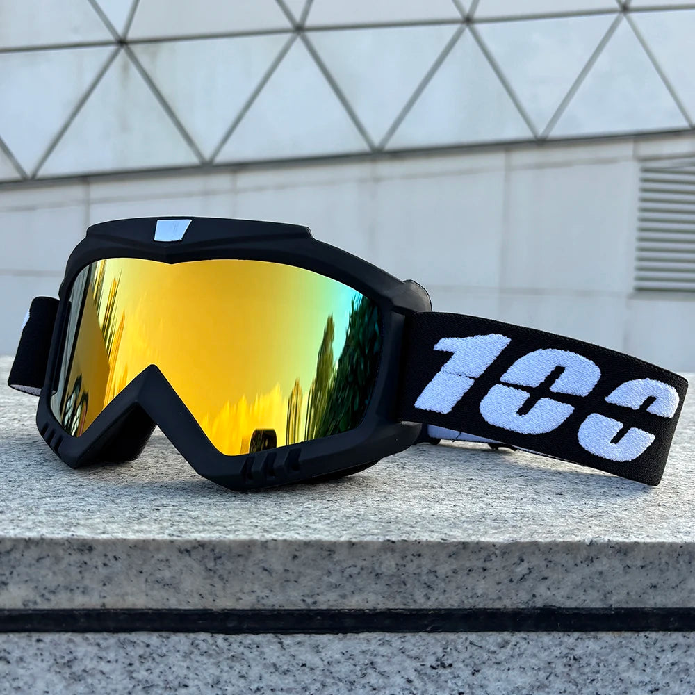 A pair of black windproof sports goggles with yellow-tinted lenses resting on a gray stone surface.