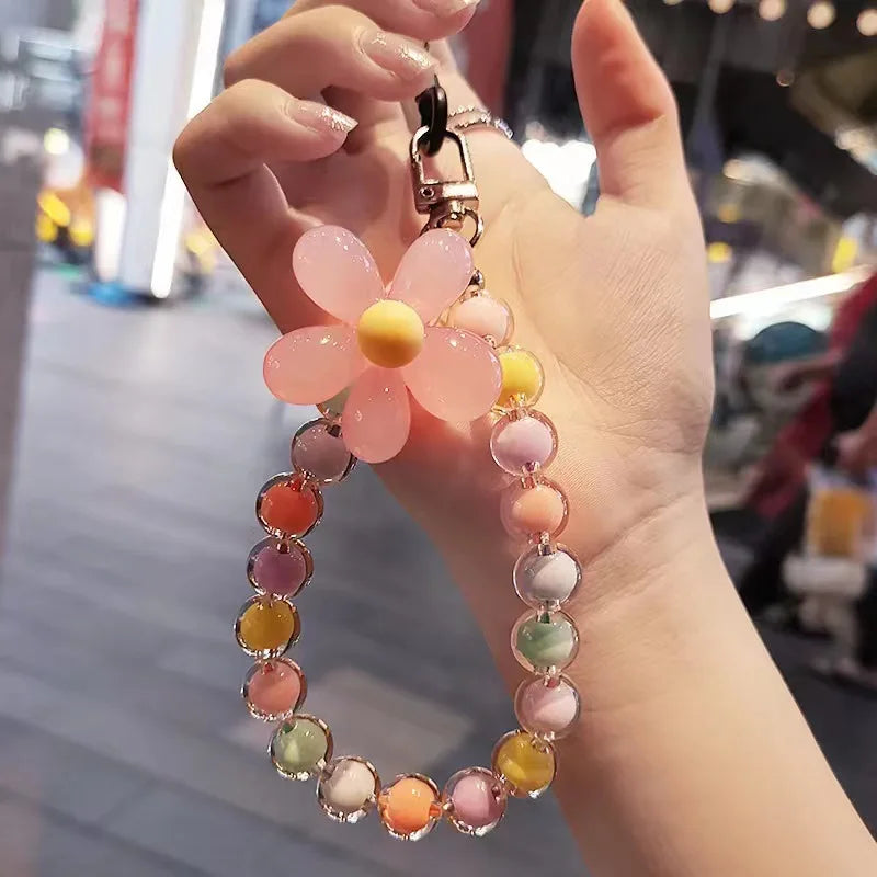 A hand holds a phone anti-loss lanyard featuring a pink flower pendant with round beads in various pastel colors.