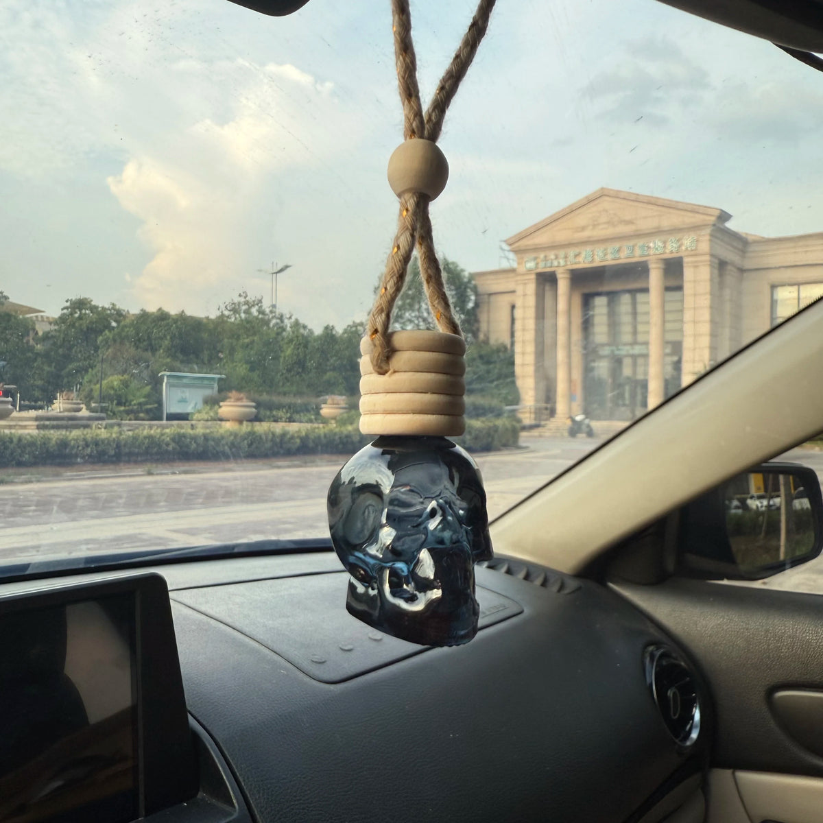 A glass skull air freshener hangs from a thick rope inside a car cabin.