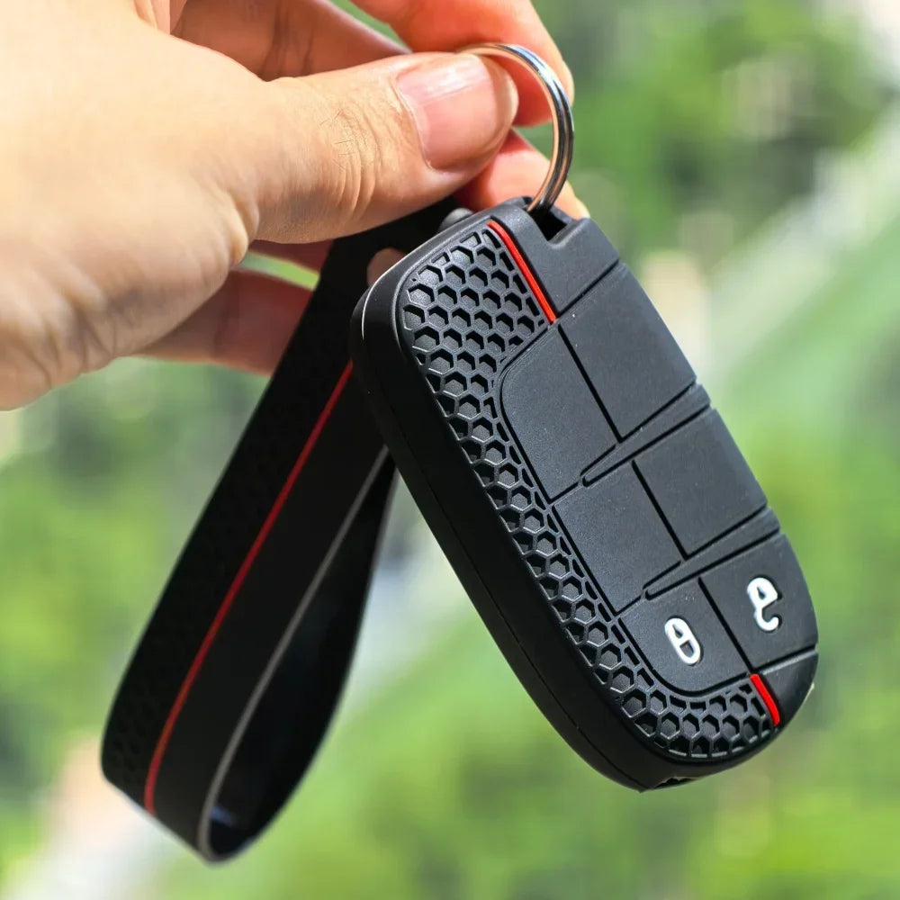 A hand is holding a black silicone car key cover with a metal ring attached, against a blurred green background.