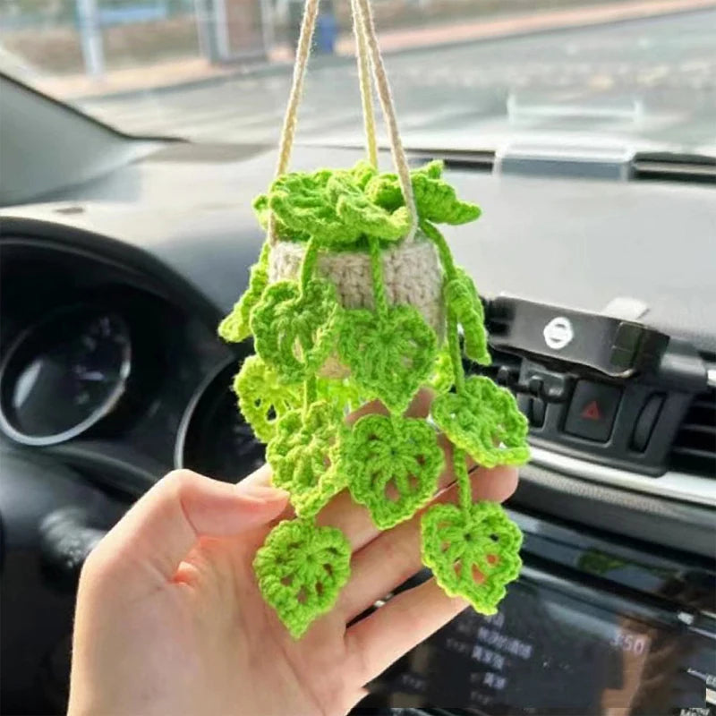 A hand holds a bright green strawberry crochet hanging decor made of yarn, placed on a car dashboard.