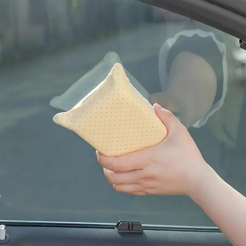 A hand holds a yellow anti-fog glass and mirror cleaning sponge against a car window.
