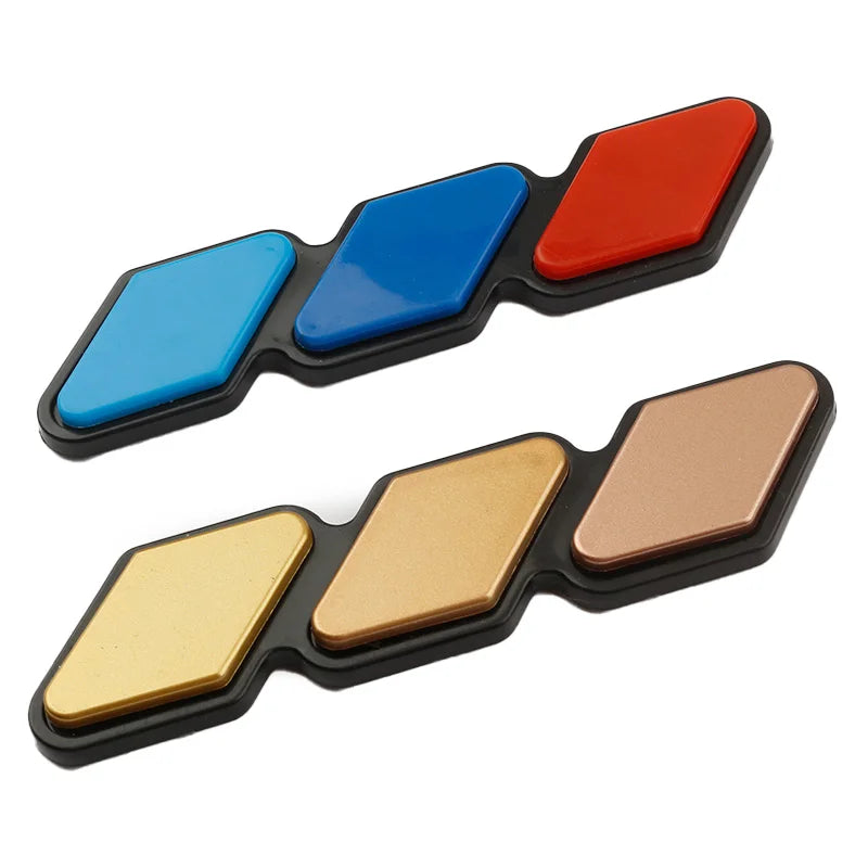 A set of three colored 3D car grill decals in red, blue, and gold.