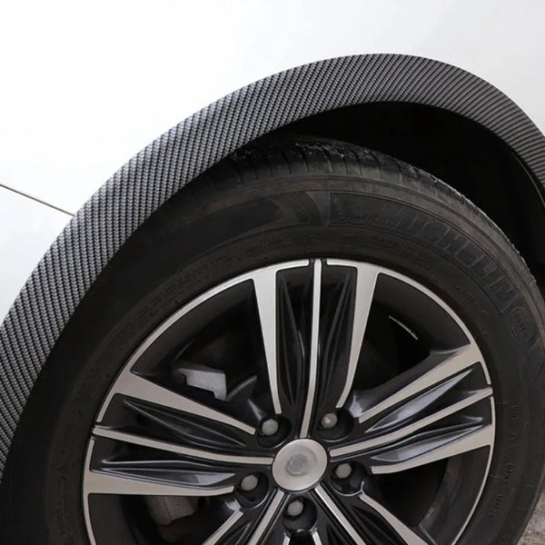Close-up view of a black carbon fiber patterned wheel arch trim and tire.