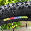 Close-up of a black tire with multi-color reflective safety stickers and spikes, mounted on a rim.