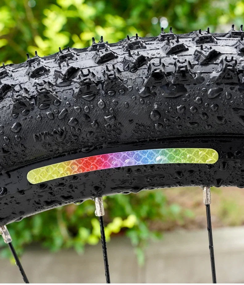Close-up of a black tire with multi-color reflective safety stickers and spikes, mounted on a rim.
