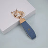 A gold-toned TPU car key fob cover with a blue leather strap and a silver chain detail.
