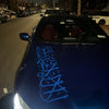 Une voiture bleu foncé décorée de stickers de calligraphie arabe bleu clair sur le capot et le pare-brise.