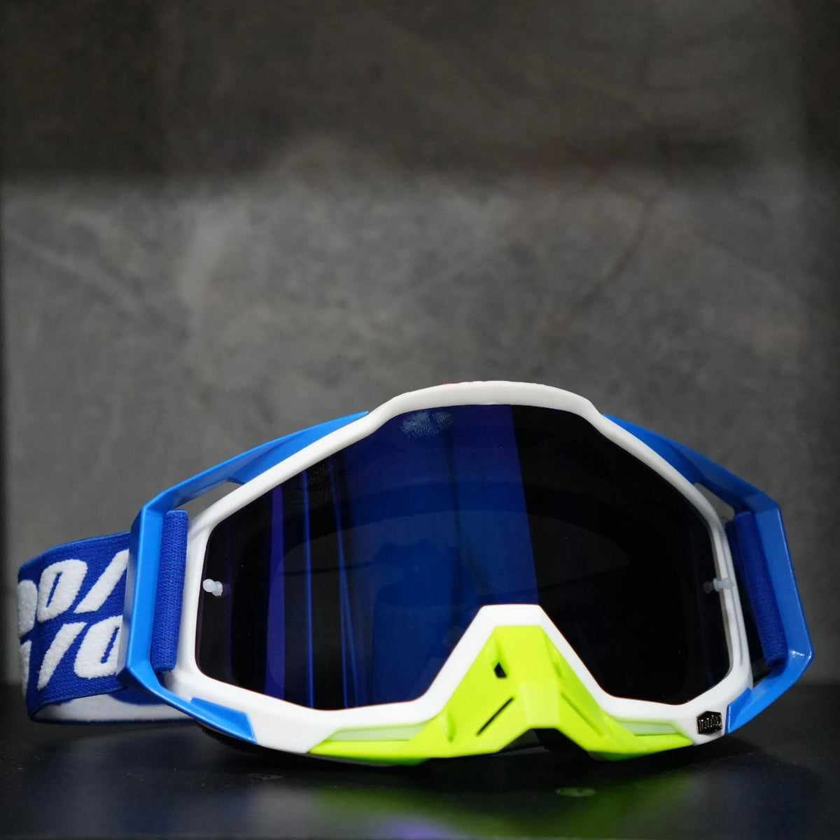 A pair of blue and white high-performance motocross goggles resting on a dark surface.