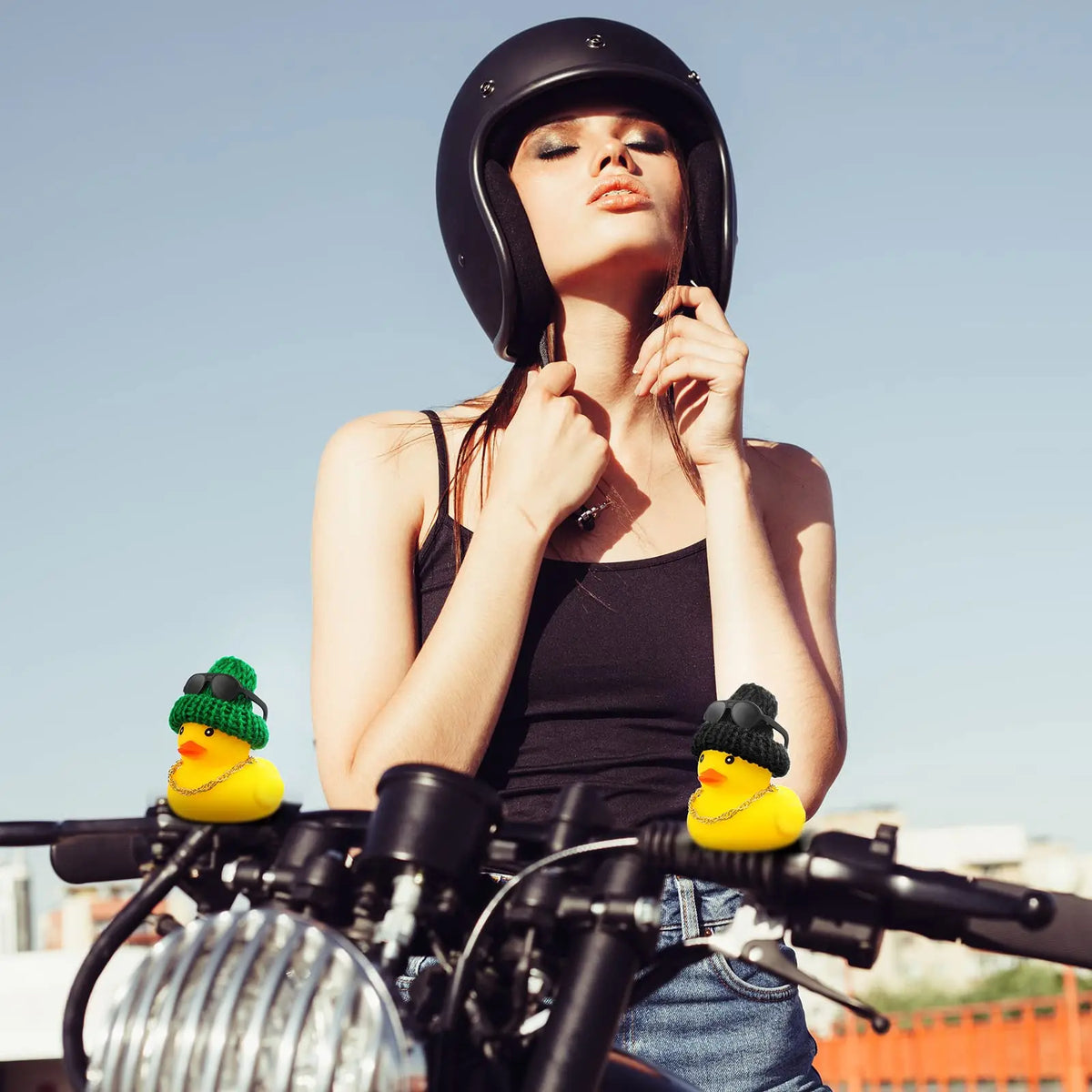 Eine Frau mit schwarzem Helm posiert mit einem Gummiduck-Auto-Dekorationsset vor einem Motorrad.