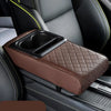 A brown quilted car armrest cushion with an integrated cup holder is shown in a vehicle interior.