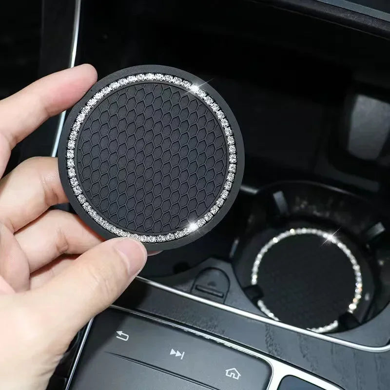 A hand holds a black silicone car cup coaster with a silver rim, placed inside a car console.