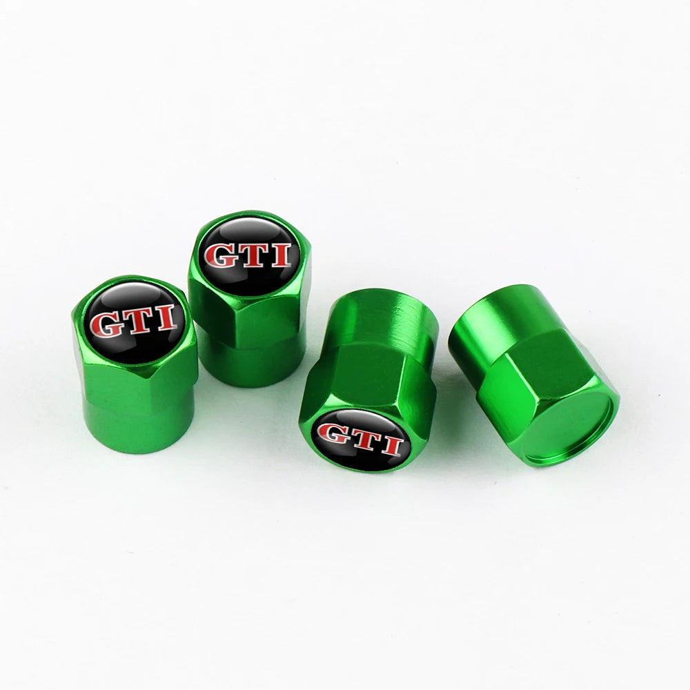 Four green metal tire valve caps with black lettering and a silver-green finish.