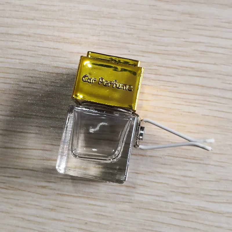 A clear glass bottle of car air freshener with a gold-colored cap resting on a light wooden surface.