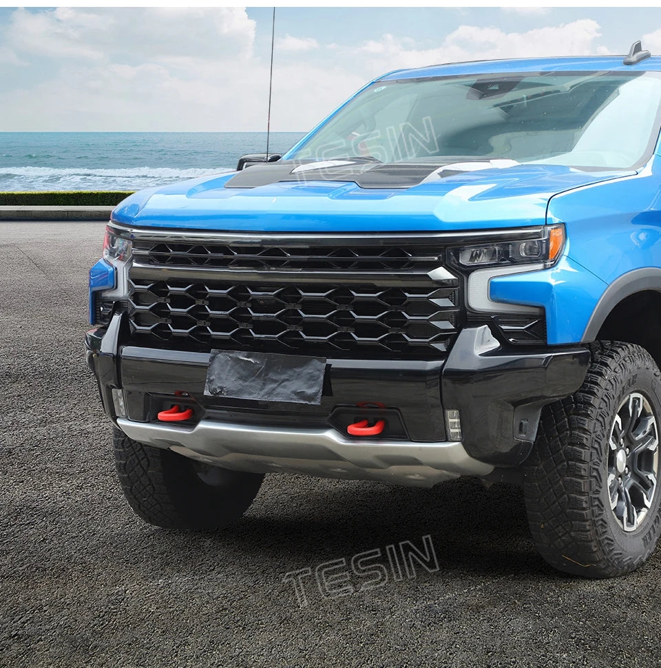 A blue Ford F-150 pickup truck with an aftermarket black bumper and tow hook cover parked on asphalt.