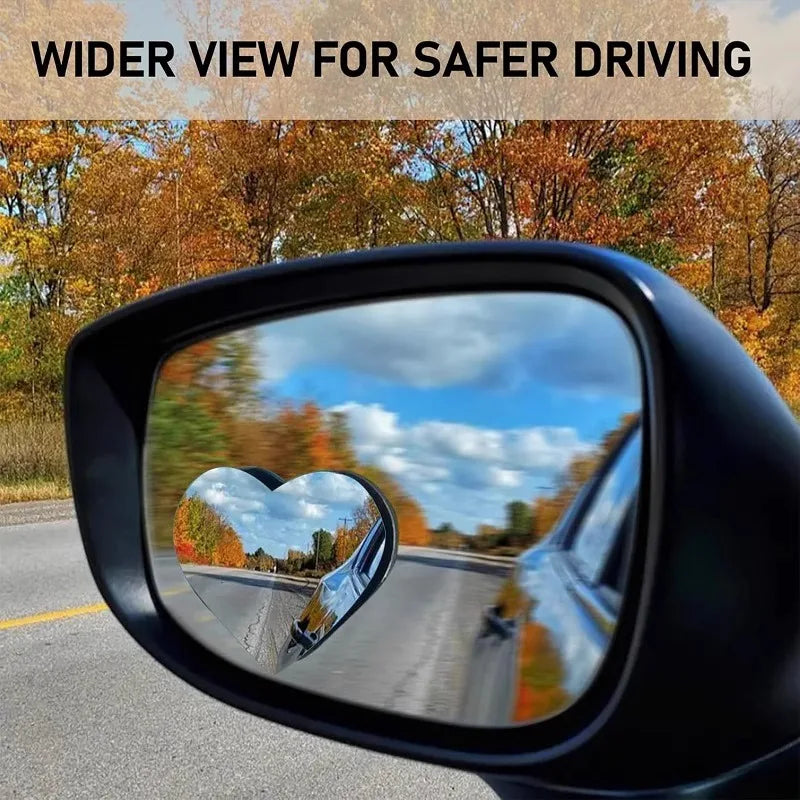 A wide view through a black heart-shaped car rearview mirror showing autumn trees and a road.