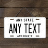 A white aluminum license plate sign with black text that reads Any State Any Text Any County, hanging from a metal chain.