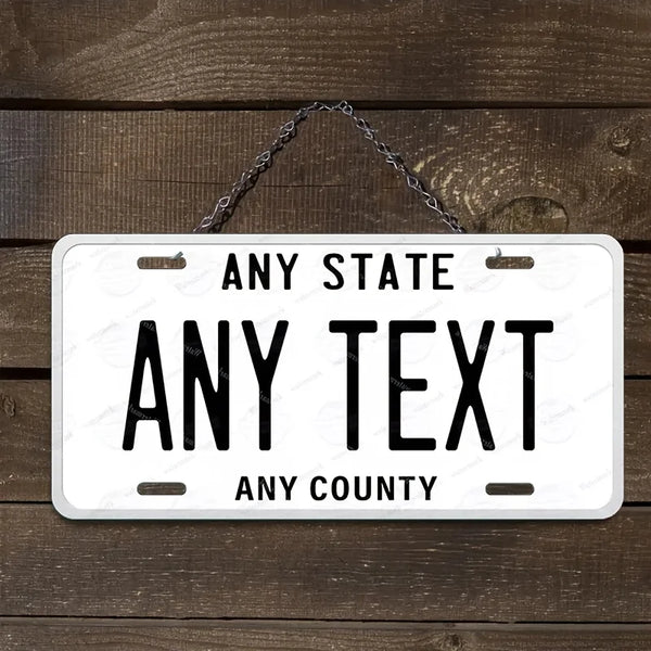 A white aluminum license plate sign with black text that reads Any State Any Text Any County, hanging from a metal chain.