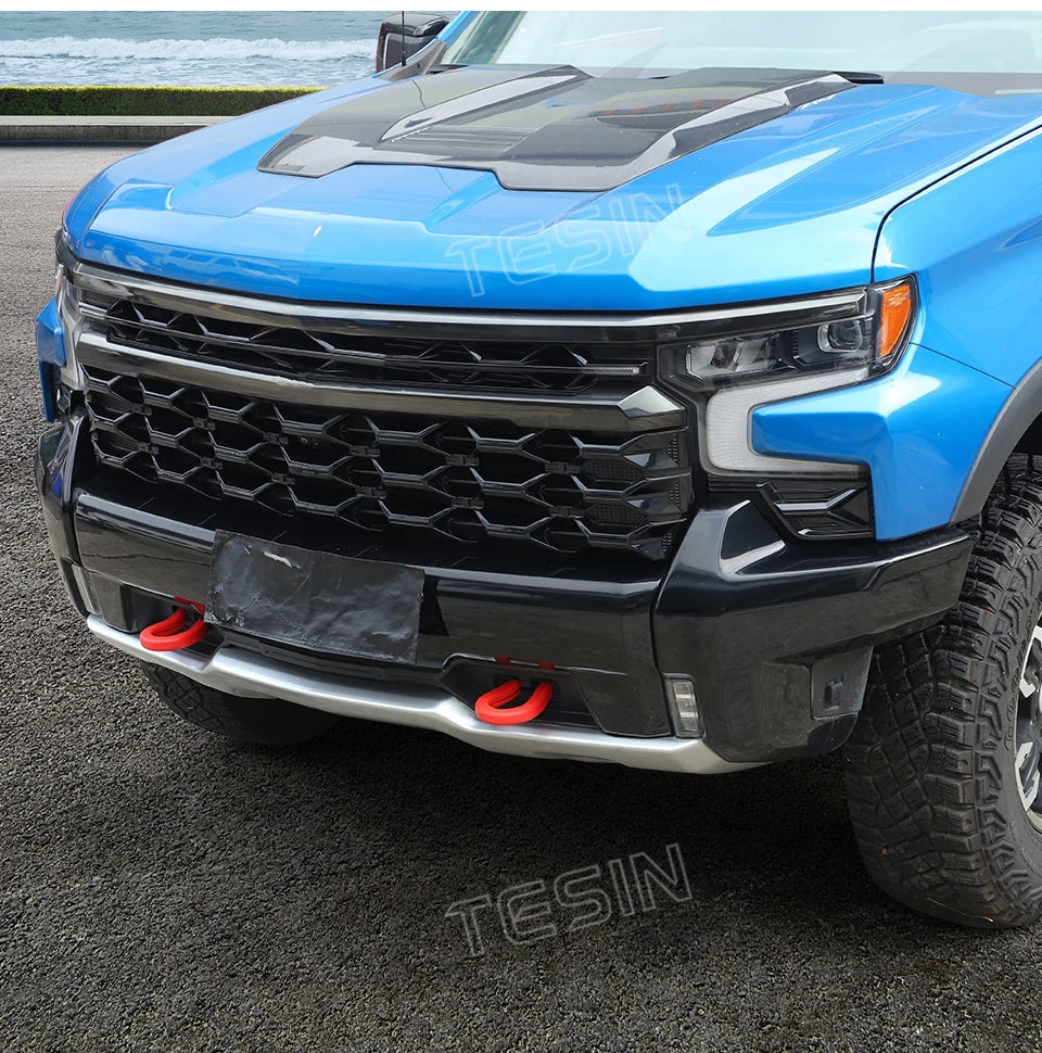 A blue pickup truck with a black grille and aftermarket tow hook covers on the front bumper.