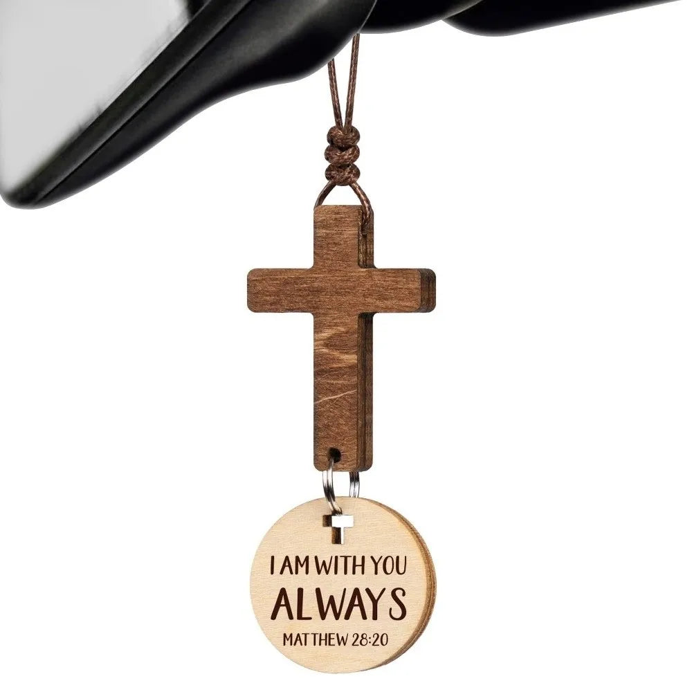 A wooden cross ornament with the inscription I AM WITH YOU ALWAYS Matthew 28:20 hanging from a black strap.