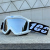 A pair of white windproof sports goggles with black strap resting on a gray stone surface.