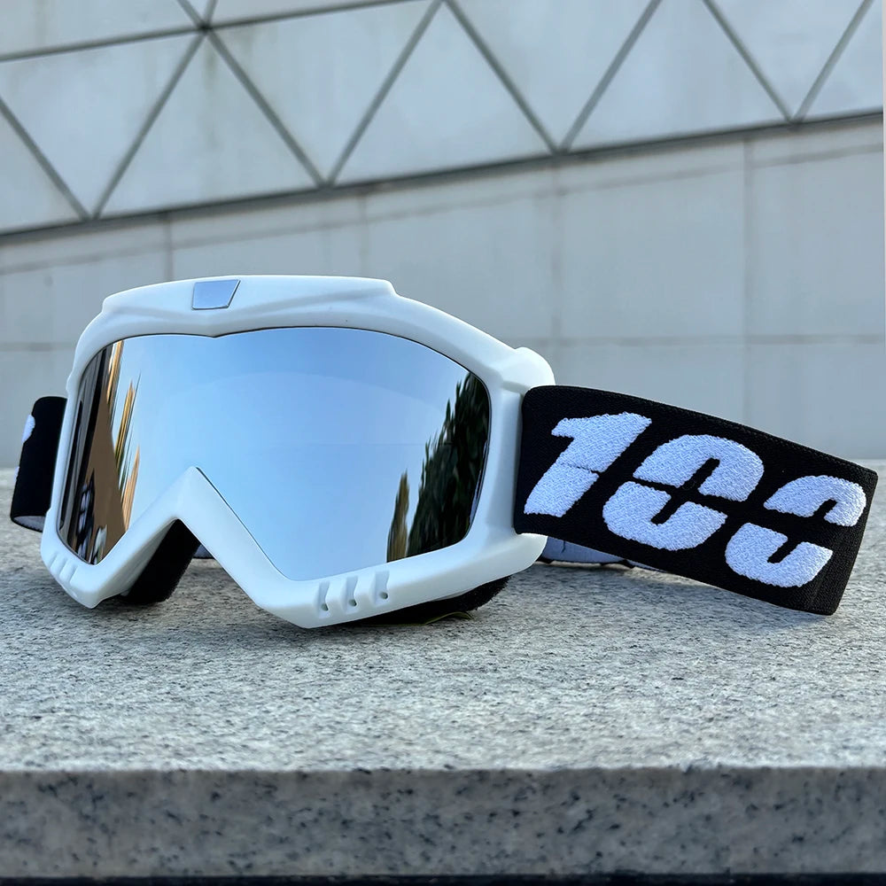 A pair of white windproof sports goggles with black strap resting on a gray stone surface.