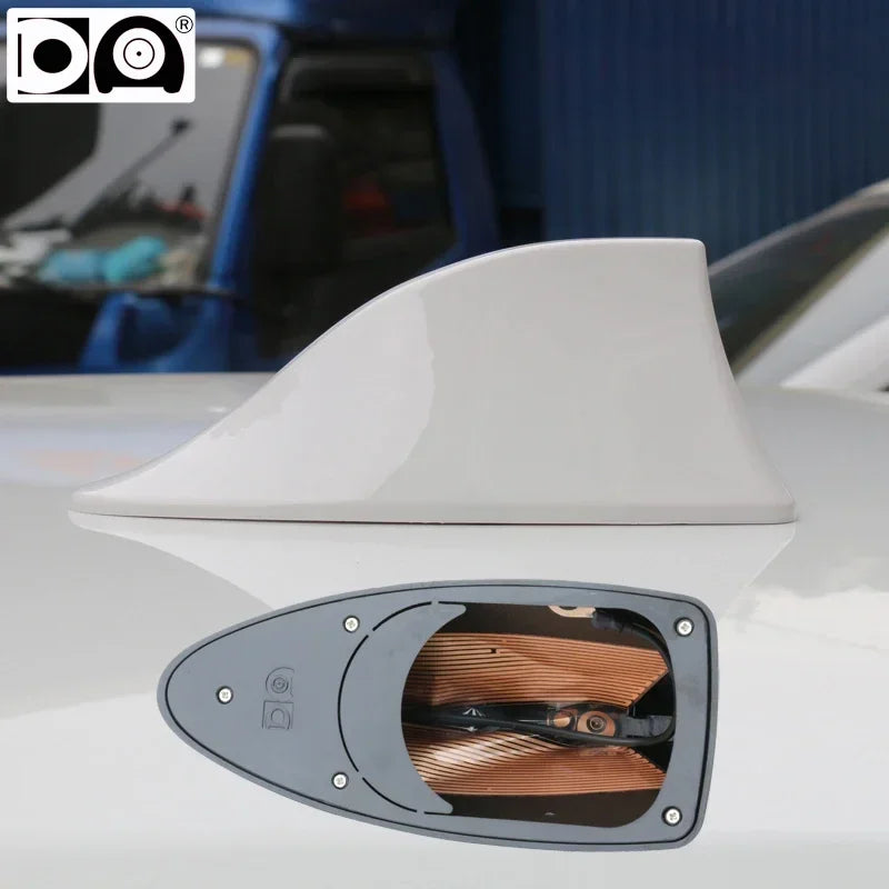 Gros plan d'une antenne de voiture avec nageoire de requin universelle, boîtier gris et câblage visible.