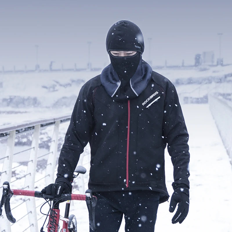 A person wearing a black thermal fleece jacket and balaclava is riding a bicycle in snowy outdoor conditions.