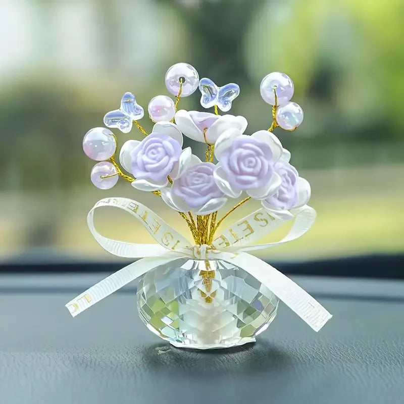 A crystal rose dashboard ornament featuring purple and white faux flowers and butterflies on a clear glass base.