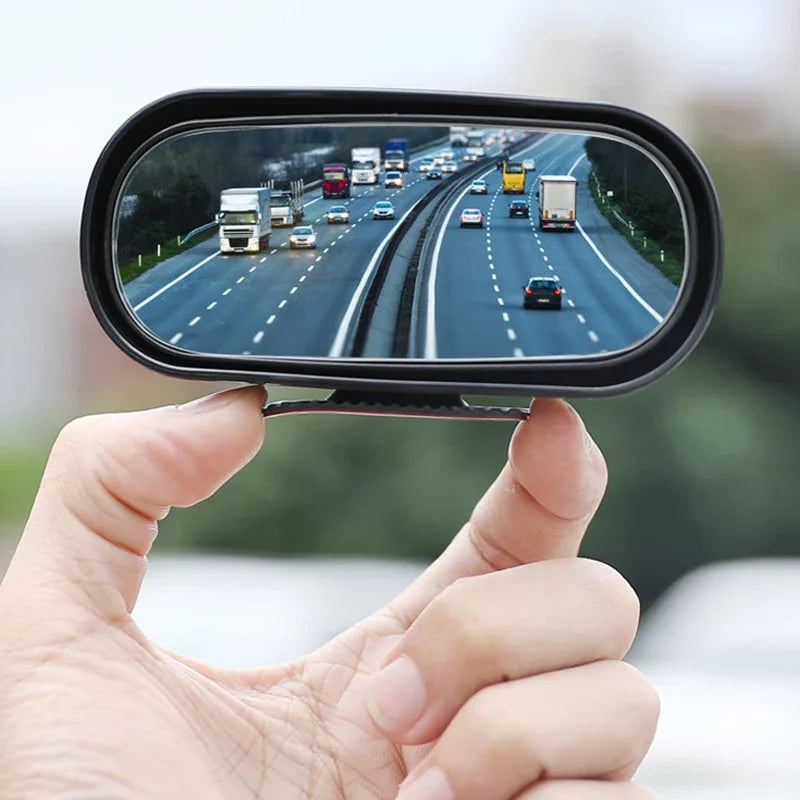 Eine Hand hält einen schwarzen 360°-Rückspiegel für das Auto, der eine Straßenansicht zeigt.