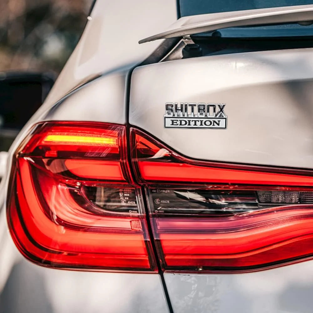 Close-up of a silver car's taillight featuring a SHITBOX EDITION logo decal.