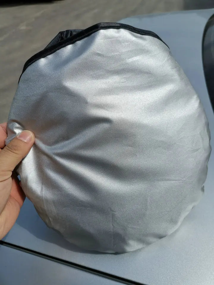 A silver folding car sunshade is being held, showing its flexible fabric and black trim.