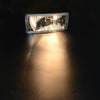 A close-up of a clear auxiliary fog light illuminating a dark surface.
