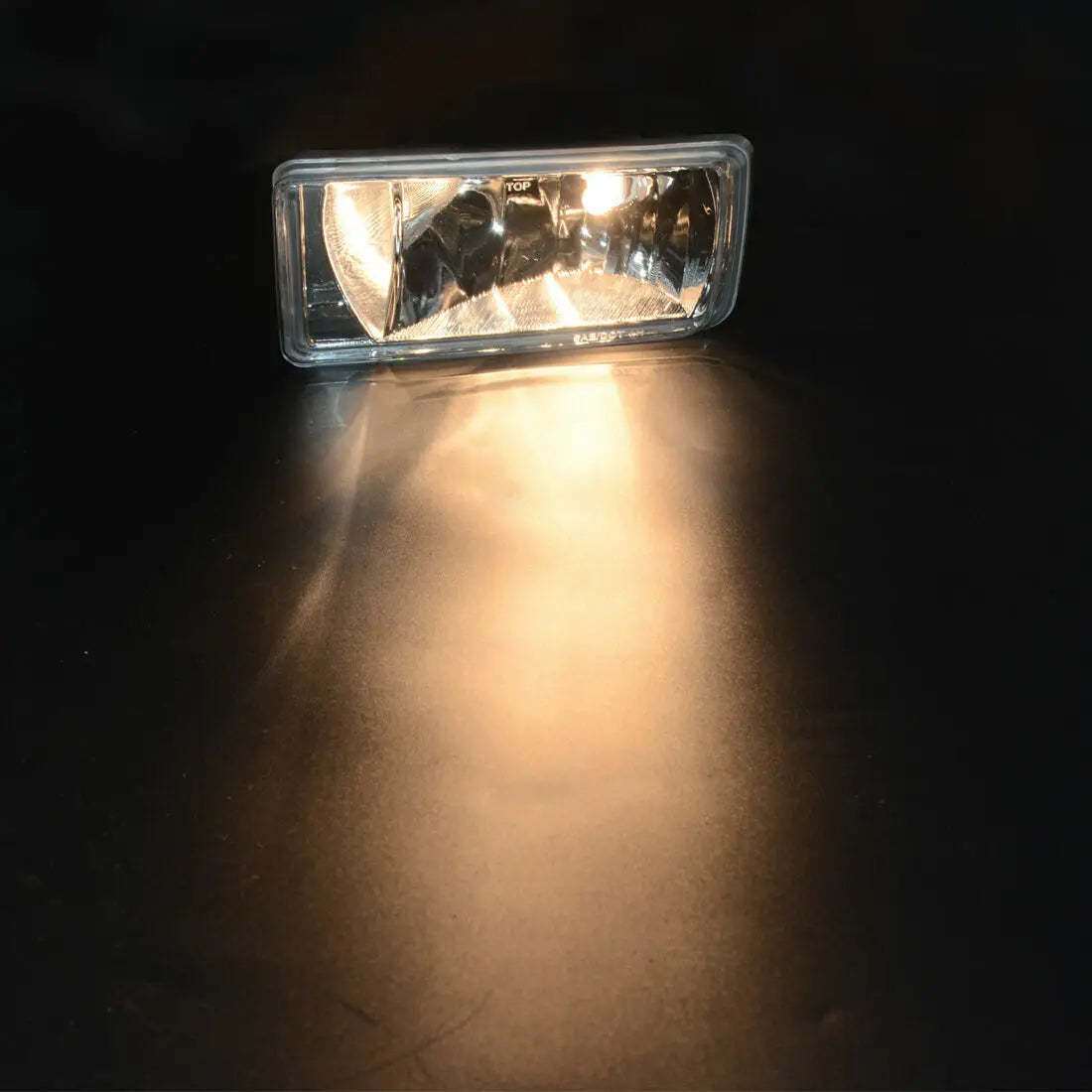 A close-up of a clear auxiliary fog light illuminating a dark surface.