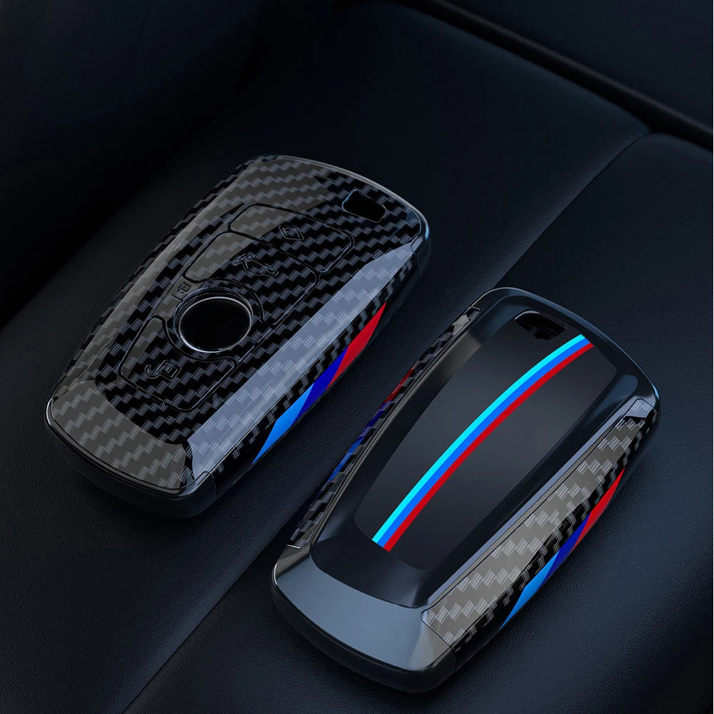 Un par de fundas para llaves de coche de fibra de carbono negra, apoyadas sobre una superficie oscura.