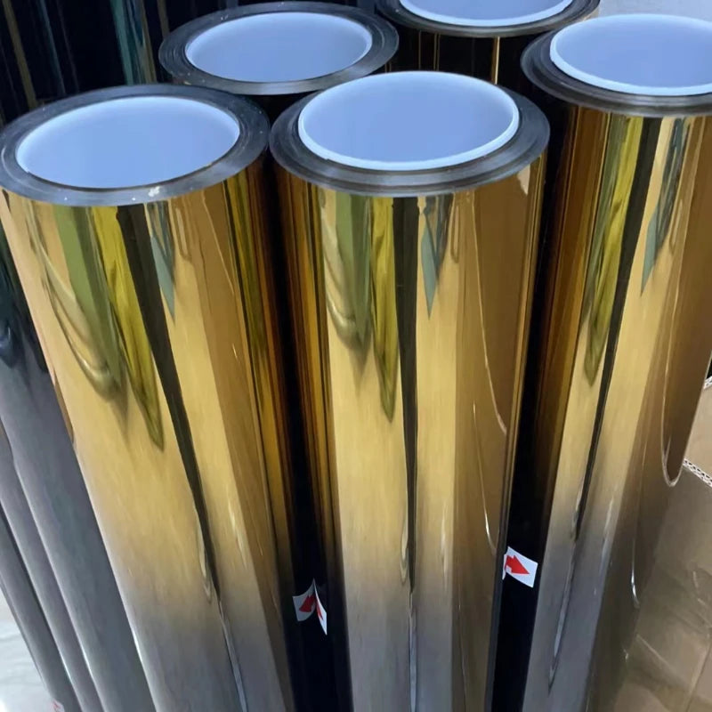 Nahaufnahme mehrerer zylindrischer Rollen von Farbverlauf-Windschutzscheibenfolie in Gold- und Silbertönen.