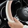 A hand is gripping a light beige perforated leather steering wheel cover inside a dark car interior.