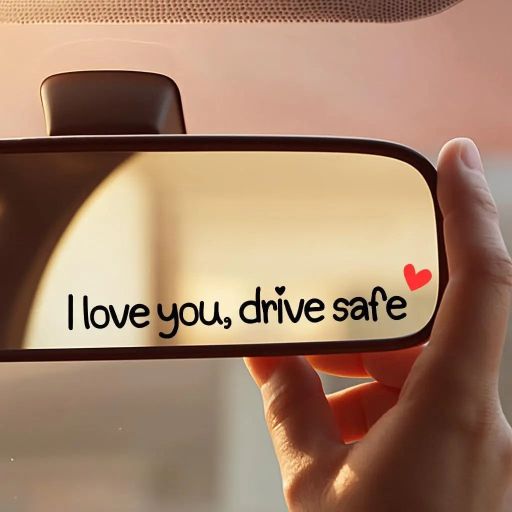 Une main tient un autocollant vinyle en forme de cœur avec le texte 'I love you drive safe' sur un arrière-plan flou.