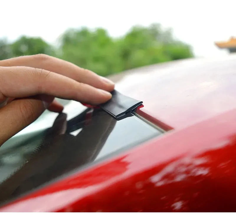 Eine Hand trägt eine schwarze Scheibenabdichtung an der Kante der Windschutzscheibe eines roten Autos auf.