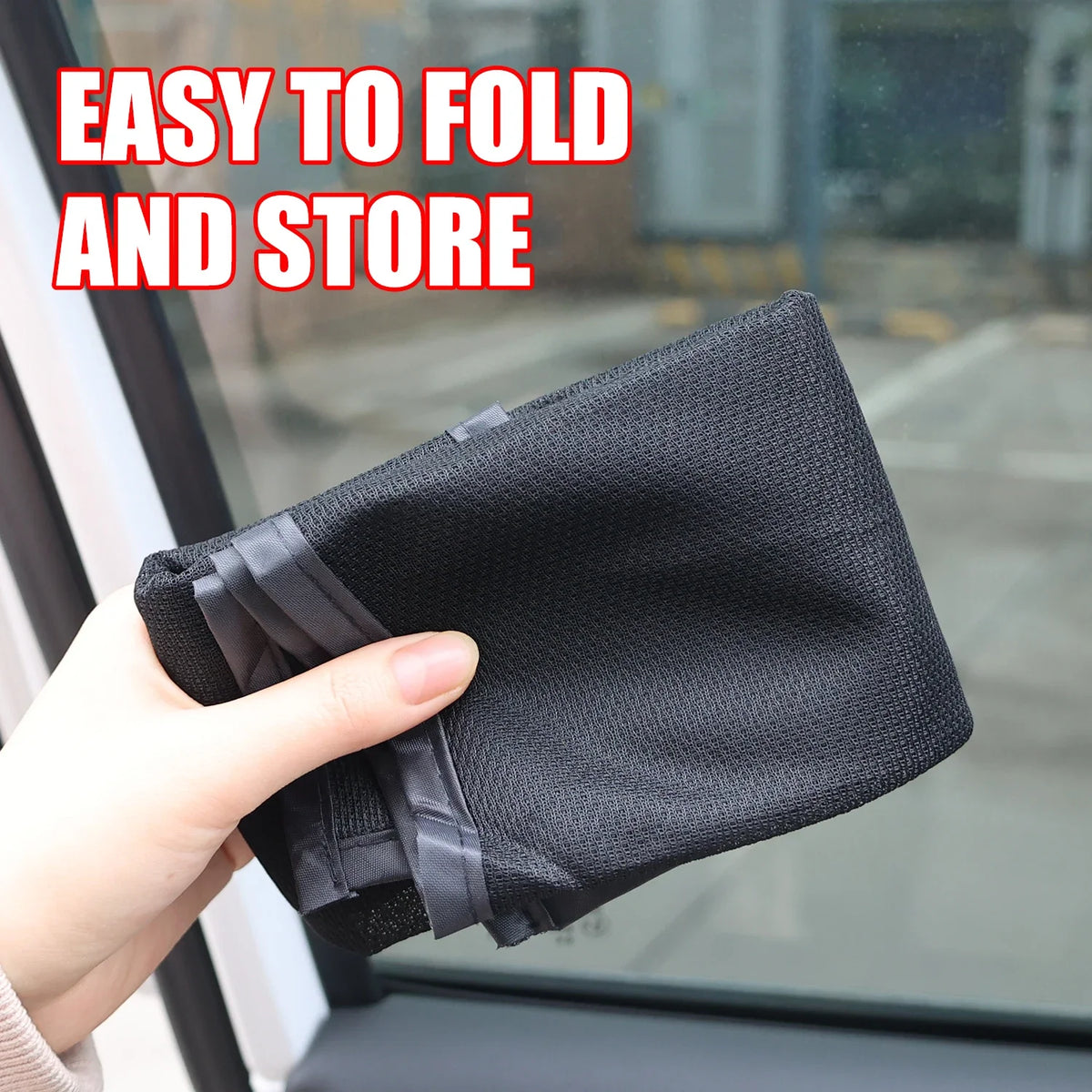 A hand is holding a black magnetic car window sunshade, demonstrating its easy to fold and store feature.