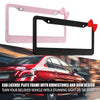 A black license plate frame with a red bow accent shown next to a pink one, set against a blurred car background.