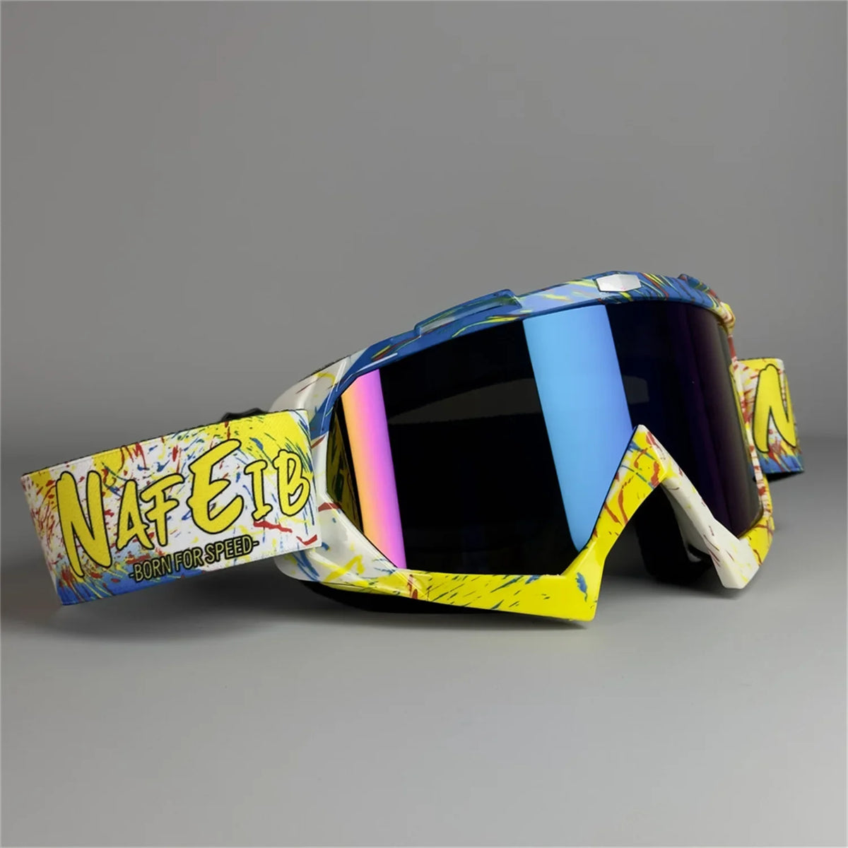 A pair of yellow and white motorcycle off-road goggles with a patterned strap resting on a gray surface.